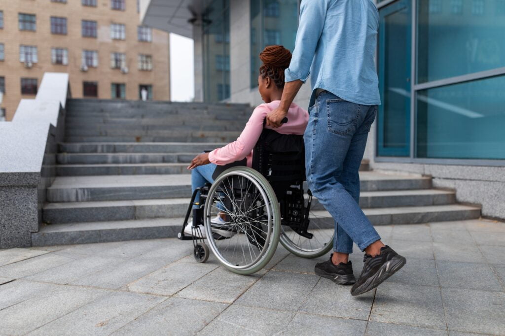 Black guy pushing wheelchair with handicapped woman, having problem entering building, standing near