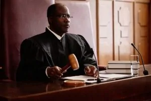 Experienced male judge with wooden gavel over sounding block sitting by desk
