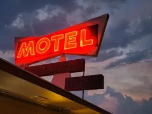Low angle shot of red neon motel sign against dark cloudy sky background